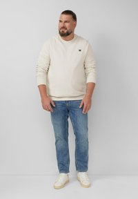 Jasno beżowy sweatshirt z długimi rękawami i ściągaczami, zestawiony z jasnoniebieskimi dżinsami i białymi trampkami z beżowymi podeszwami.