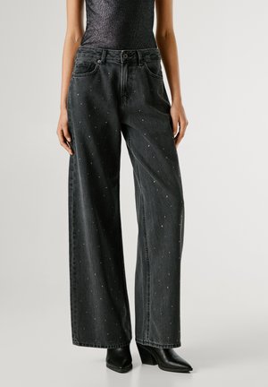 Jeans de mezclilla negra de pierna ancha, con adornos metálicos, cintura de altura media, diseño clásico de cinco bolsillos y detalles de costura en contraste.