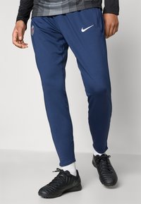 Mörkblå Nike sweatpants med elastisk midja, avsmalnande ben och sidofickor. Har en logotypapplikation på vänster lår, tillverkade av lättviktsmaterial.