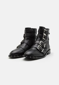 Botas de cuero negro hasta el tobillo con tres hebillas ajustables de plata, punta redondeada y suela con tachuelas. Textura suave y diseño moderno.