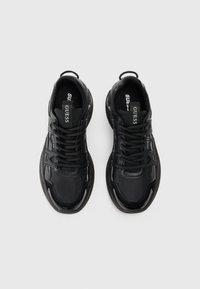 Chaussures de sport noires composées d'un mélange de cuir lisse et de mesh texturé. Présentent un design épuré, une semelle épaisse et des lacets avec des accents de marque.