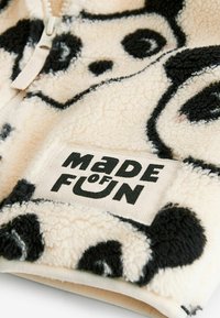 Gros plan d’un tissu en polaire doux avec un motif visage de panda et un patch cousu portant l’inscription "MADE OF FUN" en lettres noires en gras.