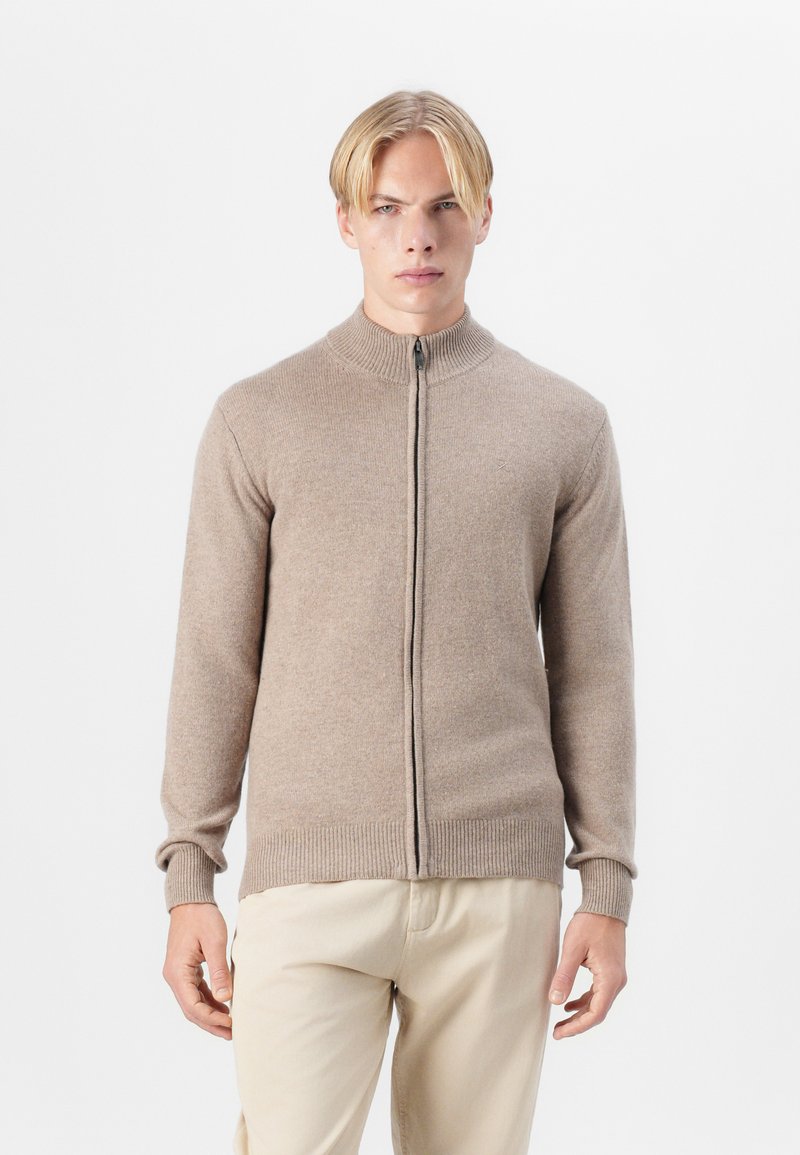 Bežna zip-up pulover s visokim ovratnikom, dolgimi rokavi in rebrastimi manšetami, izdelan iz mehkega materiala, z enostavno teksturo in minimalnim dizajnom.