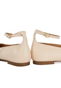 Chaussures plates en cuir verni beige avec une finition texturée, une bride à la cheville et un détail de boucle en ton doré. Talon bas avec une semelle brune lisse.