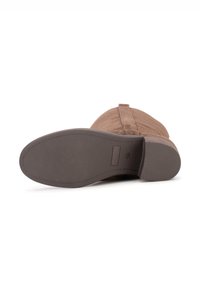 Bottine en daim marron avec une semelle en caoutchouc texturée. Présente une couture le long de l'arrière et un design simple sans ornements.