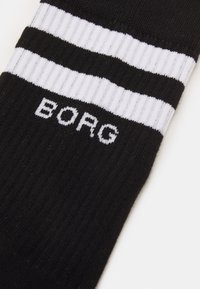 Schwarze Baumwollsocke mit weißen horizontalen Streifen und dem Wort "BORG", das in Weiß im Knöchelbereich gestrickt ist. Ribbeltextur über die gesamte Länge.