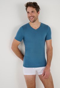 Maglietta blu a maniche corte con scollo a V realizzata in tessuto morbido, abbinata a pantaloni interni bianchi aderenti. Design semplice con una leggera lucentezza.