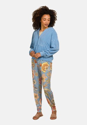 Gestreepte blauwe zip-up jas met een ontspannen pasvorm, gecombineerd met lichtblauwe broeken met een patroon van bloemontwerpen in levendige kleuren.