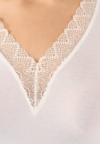 Witte V-hals top met delicate witte kant langs de halslijn en een geribbelde textuur voor extra detail.