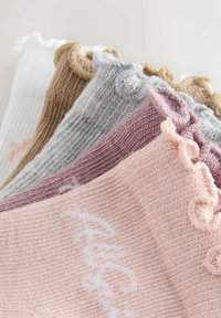 Opgestapelde gebreide sokken in pasteltinten met gerimpelde randen en subtiele geborduurde details op een lichte achtergrond.