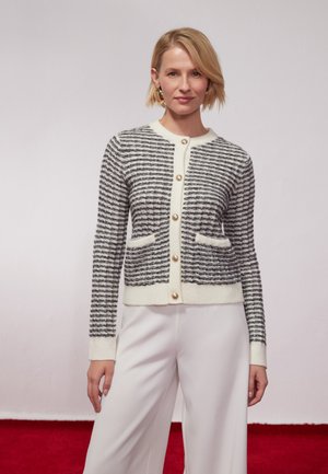 Cardigan lavorato a maglia bianco e nero con righe orizzontali, dotato di bottoni perla, due tasche frontali e collo tondo.