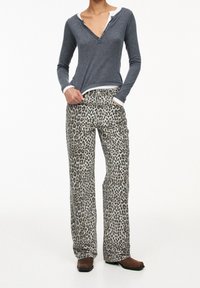 Camisa henley gris de manga larga con cuello blanco, combinada con pantalones de leopardo de pierna ancha. Tejido texturizado, ajuste casual, botas marrones hasta el tobillo.