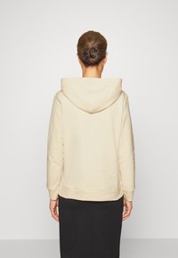 Beige hoodie met een zachte textuur, capuchon met trekkoord en geribbelde zoom. Draagt bij een zwarte rok, met zichtbare stiksels op de mouwen.