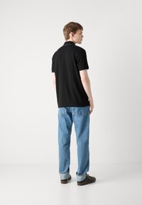 Polo nero a maniche corte, colletto standard, abbinato a jeans azzurri. L'outfit è completato da calzature marroni.