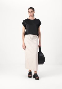 Mustapaitainen lyhythihainen paita, beige korkeavyötäröinen hame, mustat paksupohjaiset sandaalit ja musta käsilaukku. Sileä kangas minimalistisella suunnittelulla.