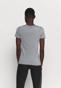T-shirt gris ajusté à manches courtes en tissu lisse. Caractérisé par un col rond et des coutures minimalistes, accompagné de leggings de sport noirs.