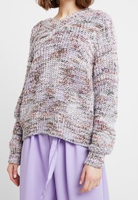 Pull en maille avec un décolleté en V, présentant un motif multicolore dans des tons de lavande doux et de crème. Coupe ample et poignets côtelés.