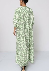 Robe longue verte et blanche avec des rayures zèbres, manches bouffantes, dos froncé et ourlet volanté. Tissu lisse avec une forme fluide.