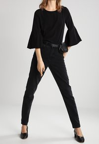 Top nero con maniche a campana abbinato a jeans neri a vita alta e tacchi neri. L'outfit presenta una vita cinchata con una piccola borsa.
