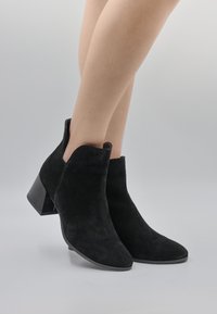Botine negre din suede, cu vârf ascuțit și toc mic p�ătrat. Designul include decupaje la glezne pentru un plus de detaliu.