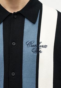 Μαύρο πλεκτό πουκάμισο με γιακά, με κάθετες μαύρες, μπλε και λευκές ρίγες και κεντημένο λογότυπο "Carhartt Wip" στο στήθος.