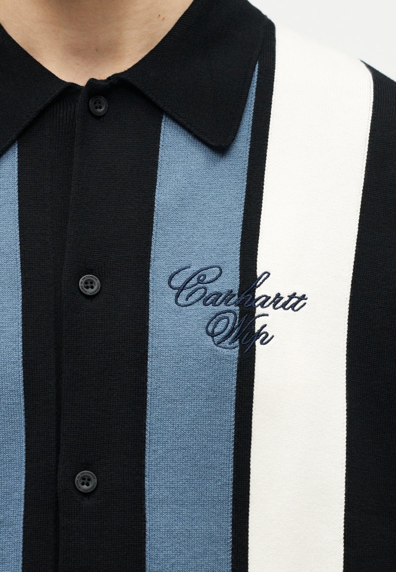 Sort strikskjorte med krave og lodrette sorte, blå og hvide striber samt broderet "Carhartt Wip"-logo på brystet.