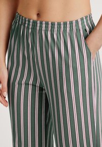 Groene gestreepte broek met een rekbare tailleband, voorzien van verticale strepen in wit en diep rood. Inclusief zijzakken voor functionaliteit.