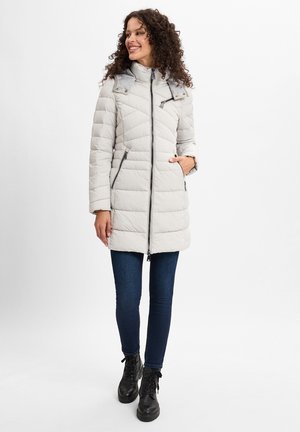 Helle graue Daunenjacke mit diagonaler Steppung, hohem Kragen, Reißverschlusstaschen und silbernen Beschlägen. Kombiniert mit dunklen Jeans und schwarzen Stiefeln.