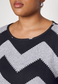 Zwart en grijs sweatshirt met een zigzagpatroon, voorzien van een ronde halslijn en textuurstof, zichtbare stiknaadaccenten en korte mouwen.