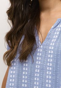 Ljusblå bomullsskjorta med vertikal vit blommönstring, V-ringning och avslappnad passform. Strukturerad tyg med subtila detaljer.