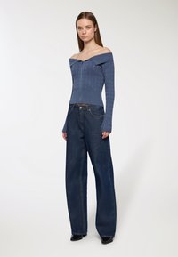 Niebieski sweter bez rękawów o wzorze warkoczowym, połączony z szerokimi ciemnymi dżinsami. Całość dopełniają botki z ostrymi noskami.