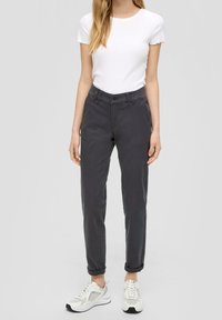 Pantalons gris retroussés avec fermeture à bouton, en coton. Associés à un t-shirt blanc et des baskets blanches.