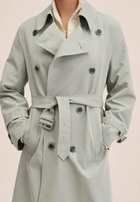 Jasnoszary trencz o podwójnym zapięciu, z dużymi guzikami i paskiem w talii. Posiada szeroki kołnierz i paski przy mankietach. Doskonały do noszenia w warstwach.