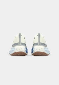 Nike sneakers with a white mesh upper, gray accents, and a textured brown sole. Features a padded collar and heel pull tabs for easy wear.