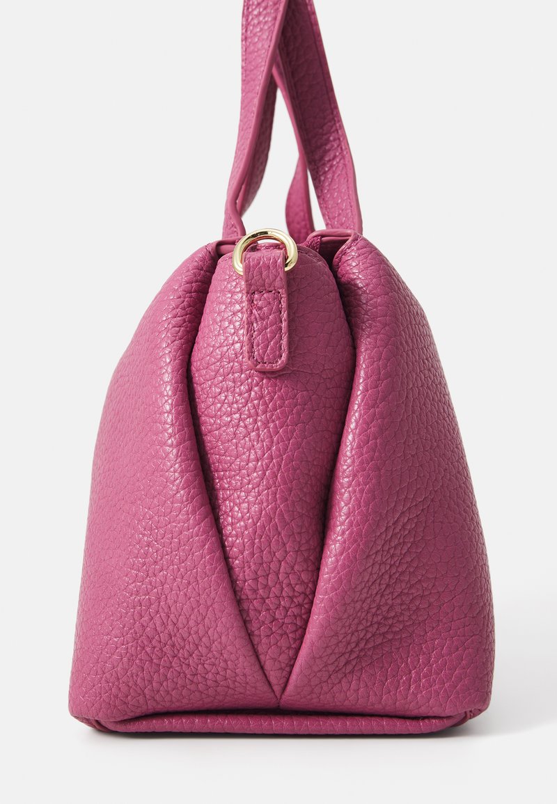 Rosa strukturiertes Lederhandtasche mit runder Form, ausgestattet mit einem goldenen Hardware-Ring und einem einzelnen Tragegurt. Auffälliges Faltendesign an der Vorderseite.