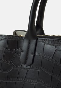 Svart läderhandväska med krokodilstruktur, med dragkedjestängning och två robusta handtag. Anmärkningsvärd sömdetalj förbättrar designen.