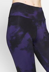 Legginsy w wysokim stanie w kolorze fioletowym z czarnym wzorem plam. Wykonane z elastycznej tkaniny, z gładką, dopasowaną sylwetką i szytymi detalami.
