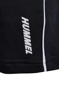 Svarta sportshorts med vitt varumärkeslogotyp "HUMMEL" och diskret vit sidostrand. Tillverkade av texturerad, stretchig tyg.