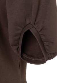 Braunes Kleidungsstück mit einer runden Ärmeln und Raffung am Ellenbogen, gefertigt aus glattem, dehnbarem Stoff.