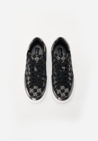 Μαύρα αθλητικά παπούτσια με υφή, που διαθέτουν επαναλαμβανόμενο μοτίβο λογότυπου σε ασημί. Οι χοντρές λευκές σόλες και οι μαύρες κορδόνες ολοκληρώνουν το σχέδιο.