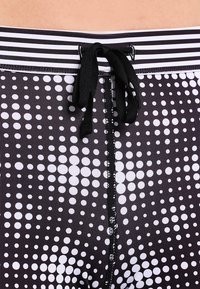 I pantaloni corti a righe bianco e nero presentano un motivo a pois di dimensioni variabili. La vita a righe ha un cordino nero e una cucitura visibile.