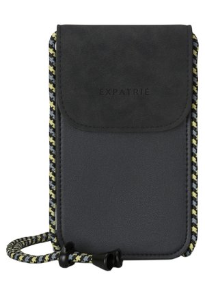 Kompakti musta olkalaukku, jossa on teksturoitu läppä, "EXPATRIÉ" painettuna ja monivärinen punottu säädettävä hihna.