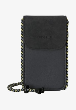 Pequeño bolso cruzado negro con solapa texturizada, con la palabra "EXPATRIÉ" en relieve y correa ajustable trenzada multicolor.