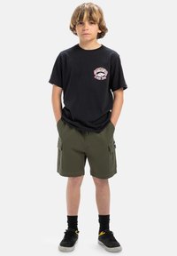Svart bomullströja med rosa grafisk tryck på bröstet, kombinerad med olivgröna cargoshorts. Svarta strumpor och skor fulländar looken.