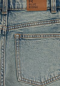 Nærbillede af baglomme på blå denimjeans med orange søm og en brun læderlap med teksten "Blue Ridge."
