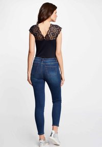 Mustat yläosa, jossa on pitsiyksityiskohta selässä, yhdistetty tummansinisiin slim fit -farkkuihin. Mallilla on päällään hopeiset tennarit. Sujuva kangas, tiukka malli.