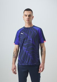 Mornarsko modra in vijolična športna majica s kratkimi rokavi z abstraktnim vrtinčastim vzorcem ter kontrastnimi roza poudarki na rami. Vključuje PUMA logo.