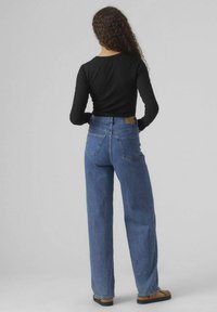 Hoch taillierte blaue Jeans aus Denim mit geradem Schnitt, strukturiertem Stoff und zwei Gesäßtaschen. Kombiniert mit einem enganliegenden schwarzen Langarmtop.
