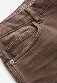 Jeans de denim maroș cu o finisare texturată, dotate cu un buzunar posterior și cusături contrastante, evidențiate de un detaliu cu nit metalic.