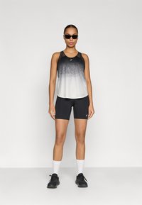 Μαύρη και γκρι αθλητική μπλούζα χωρίς μανίκια με λεπτομέρειες από δίχτυ, συνδυασμένη με μαύρο σορτς και λευκές κάλτσες αστραγάλου. Το μοντέλο φοράει μαύρα γυαλιά ηλίου και παπούτσια για τρέξιμο.